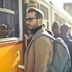 A stylish man with a backpack boards a tram in bustling Budapest, Hungary, during the day.